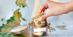 Collecting money for travel. Glass tin as moneybox with cash (Photo via Aksenovko / iStock / Getty Images Plus)