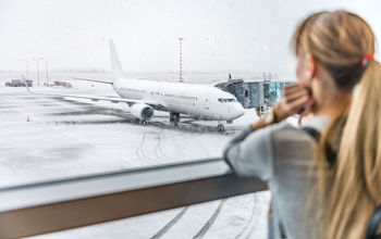 Woman gazing at snowy tarmac and delayed plane flight.