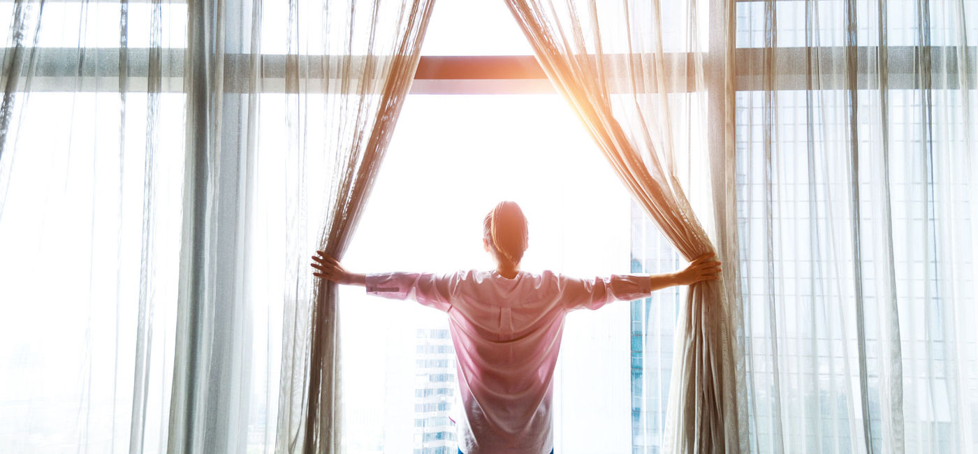 Image: PHOTO: Woman at window with curtains. (Photo via iStock / Getty Images E+ / baona)