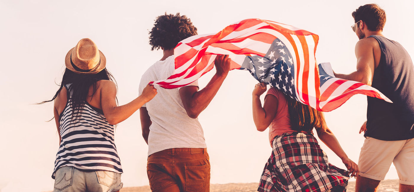 Image: Friends with American flag. (photo via g-stockstudio / iStock / Getty Images Plus)