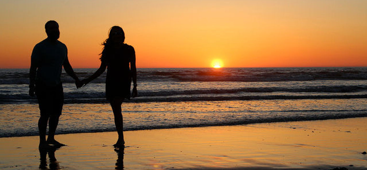 Image: PHOTO: A couple in silhouette holding hands on a beach. (photo via Flickr/Nicole June)