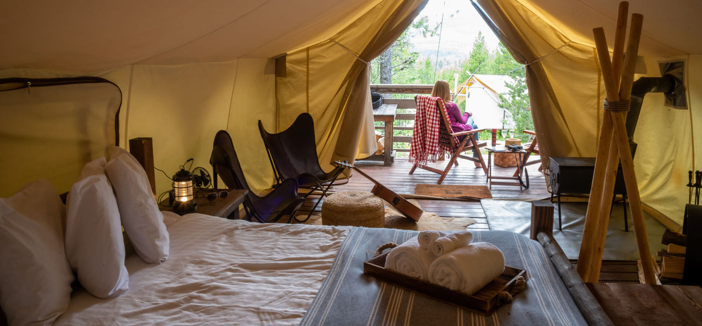 Image: Woman sitting outside luxury tent on glamping trip in Glacier National Park (Photo via DavidPrahl / iStock / Getty Images Plus)