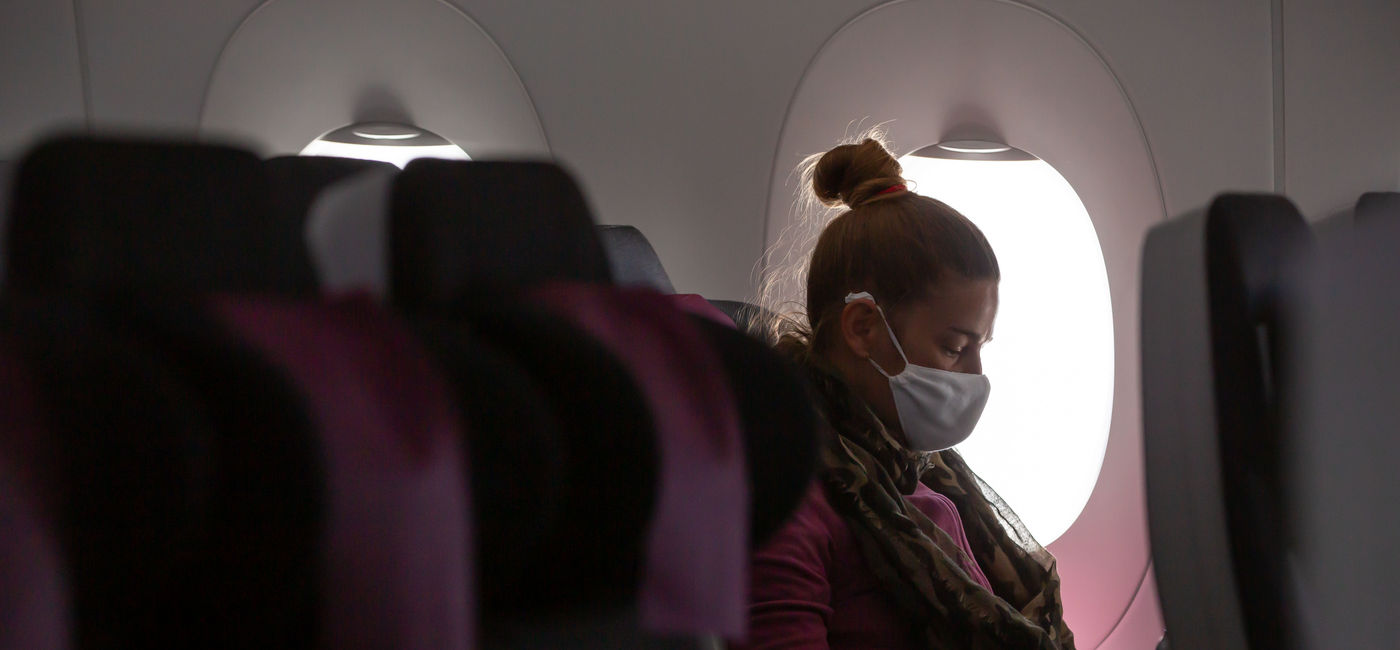 Image: A woman wearing a face mask on an airplane. (photo via exithamster / iStock / Getty Images Plus)
