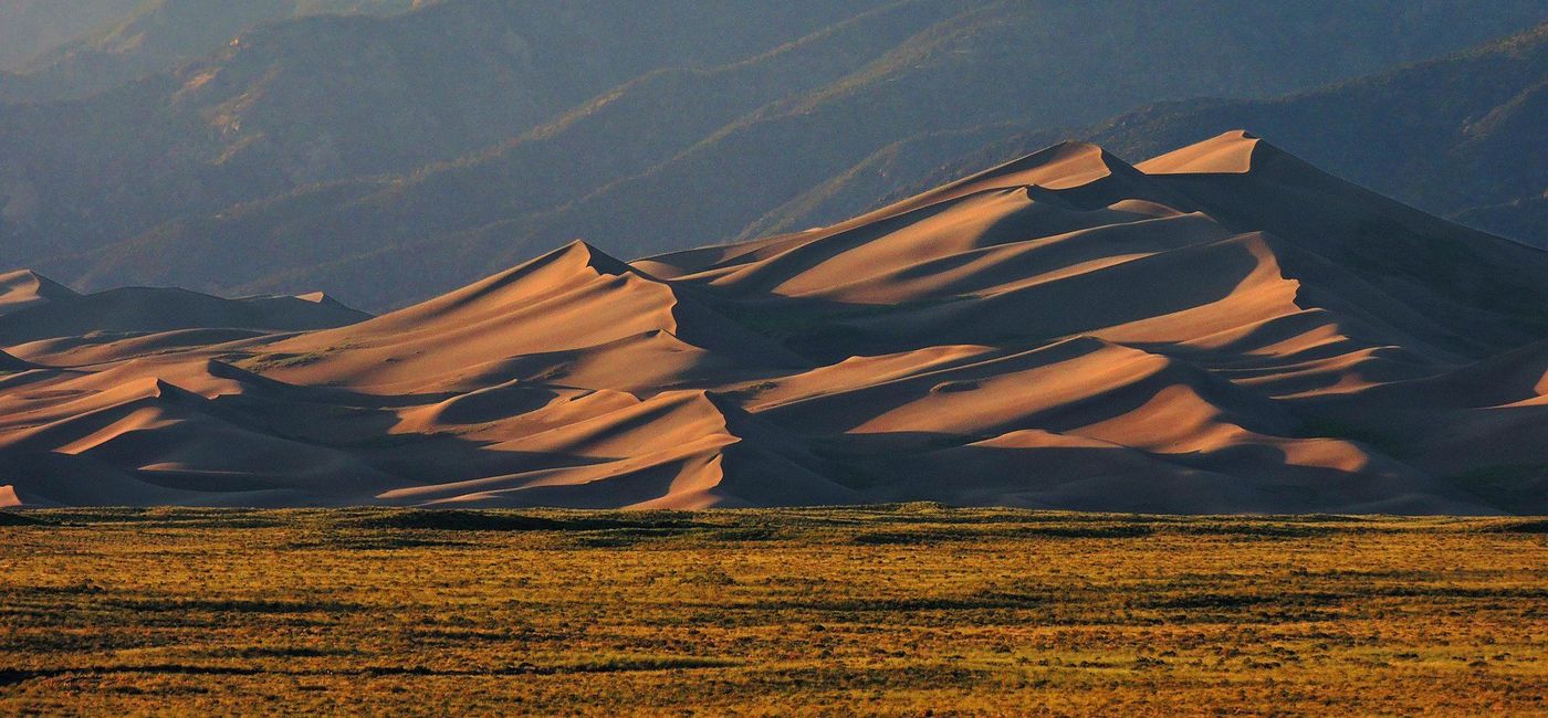 Image: PHOTO: The force of wind can be seen in the sculpted shapes of the huge dunes rising below the Sangre de Cristo Mountains. (Photo via Alamosa Convention and Visitors Bureau)