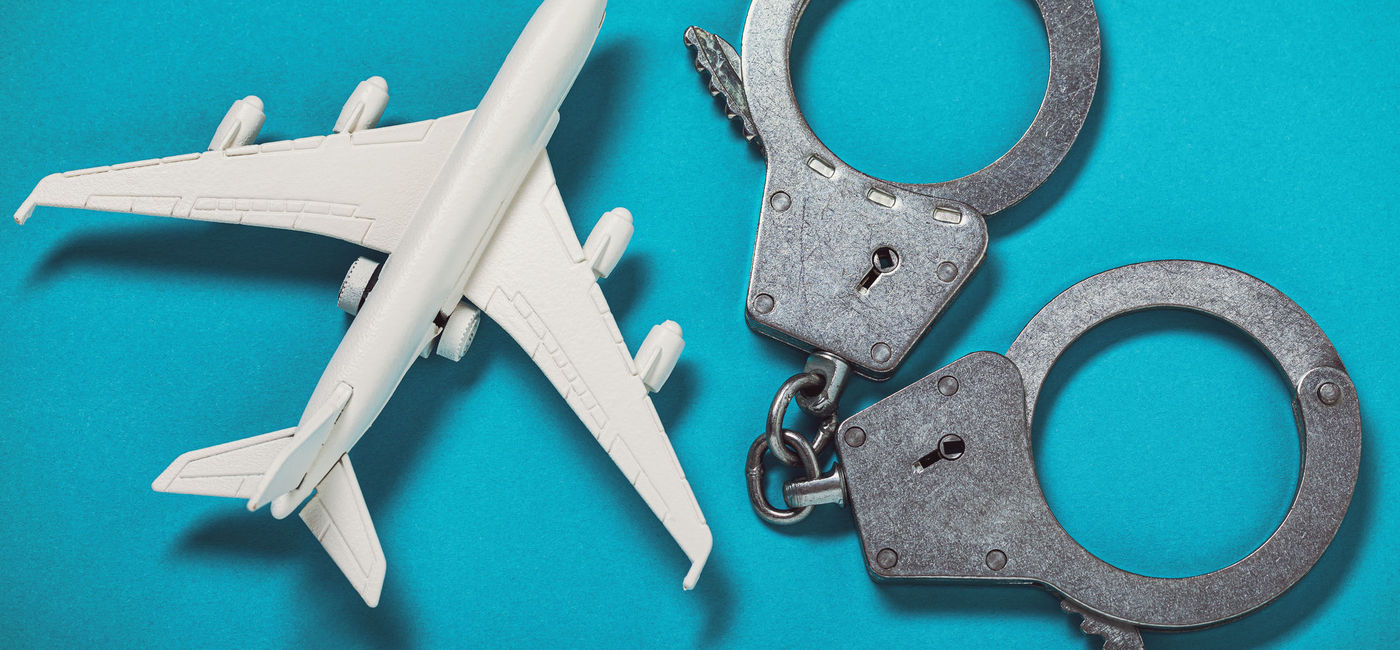 Image: Airplane and handcuffs on the table. (photo via SergeyChayko / iStock / Getty Images Plus)