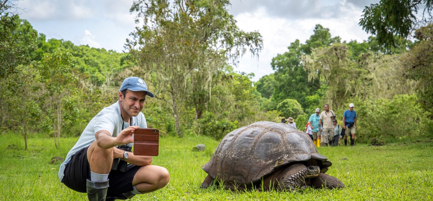 Image: A man crouches near a Galapagos giant tortoise. (photo via Ashton Ray Hansen) ((photo via Ashton Ray Hansen))