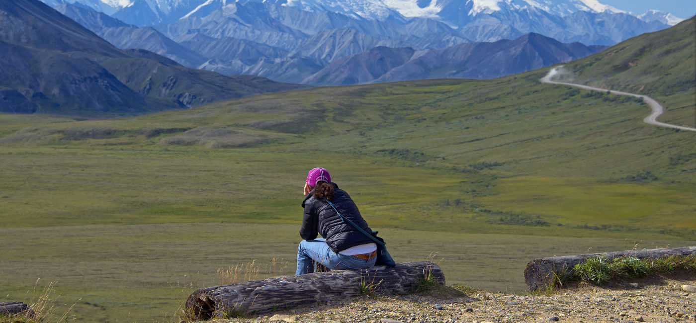 Image: A person sits below a mountain in Alaska. (Photo Credit: Holland America Line)