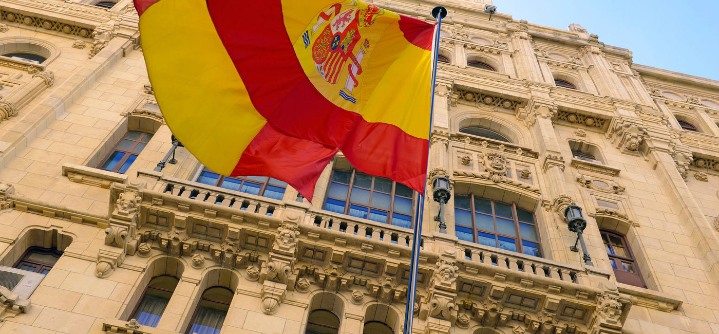 Image: The Spanish flag flying in front of a building in Madrid. (photo via iStock/Getty Images Plus/robertcicchetti)