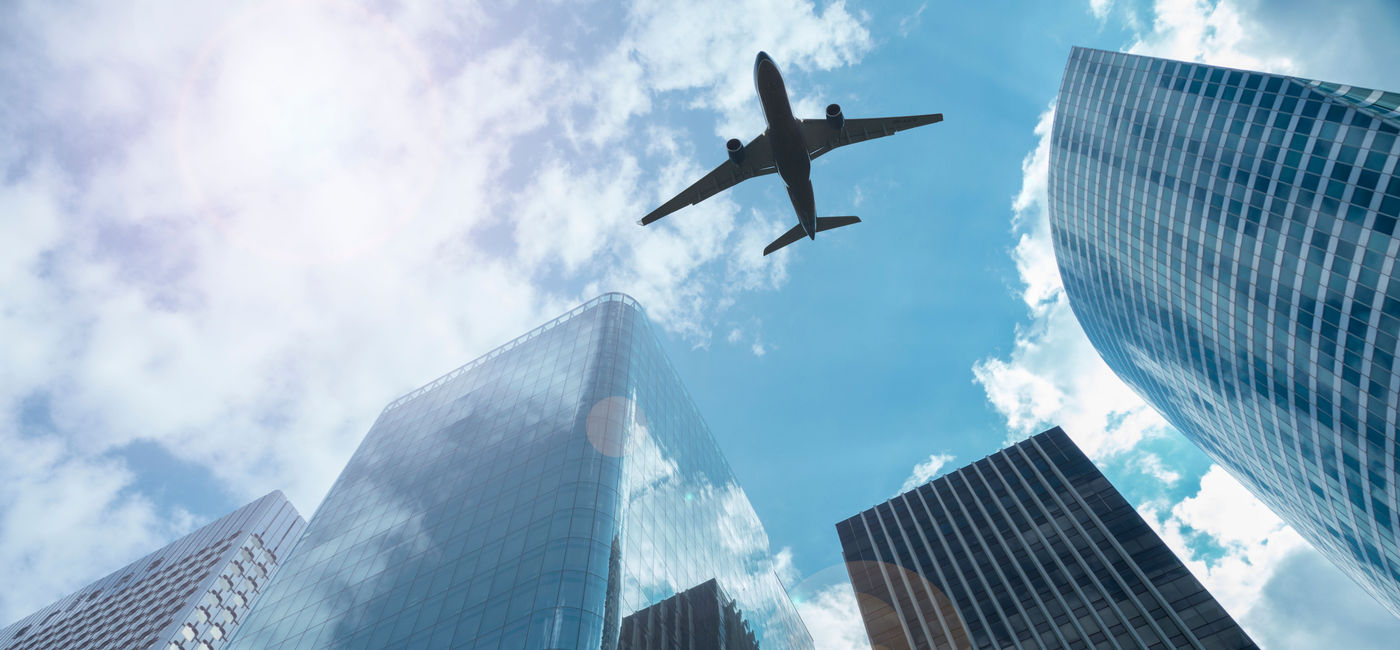 Image: Airplane in the sky over modern buildings. (photo via Simonkolton/iStock/Getty Images)