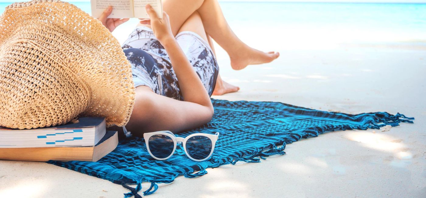Image: PHOTO: Woman reading a book on the beach. (photo via Yumi mini/iStock/Getty Images Plus)