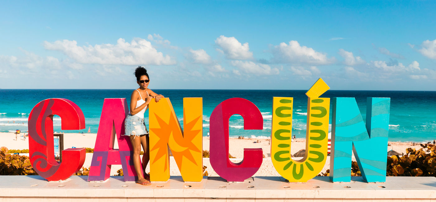 Image: Woman poses at Cancun sign in Mexico (photo via MediaProduction / iStock / Getty Images Plus)