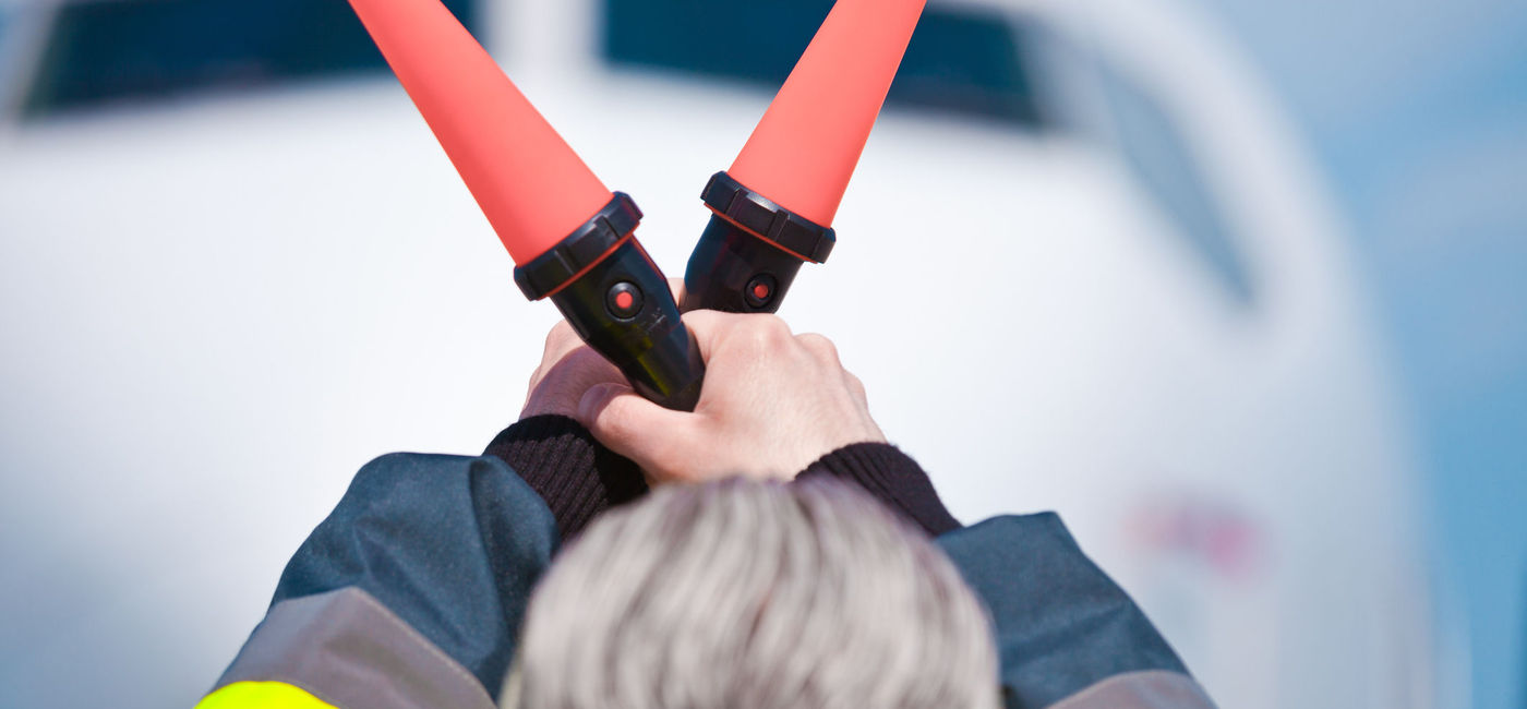 Image: Ground control worker waving air traffic signals on an airport runway.  (Source: iStock/Getty Images Plus/izusek)