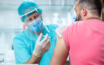 Doctor wearing PPE administering vaccine to a patient.