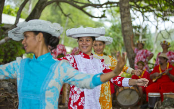 Local women in colorful dresses dance on the island of Rurutu