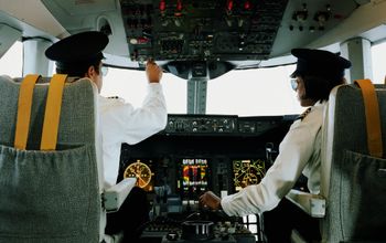 Male and female aeroplane pilot, operating controls, rear view
