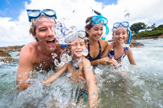 A family wearing snorkels play in the waves on the beach