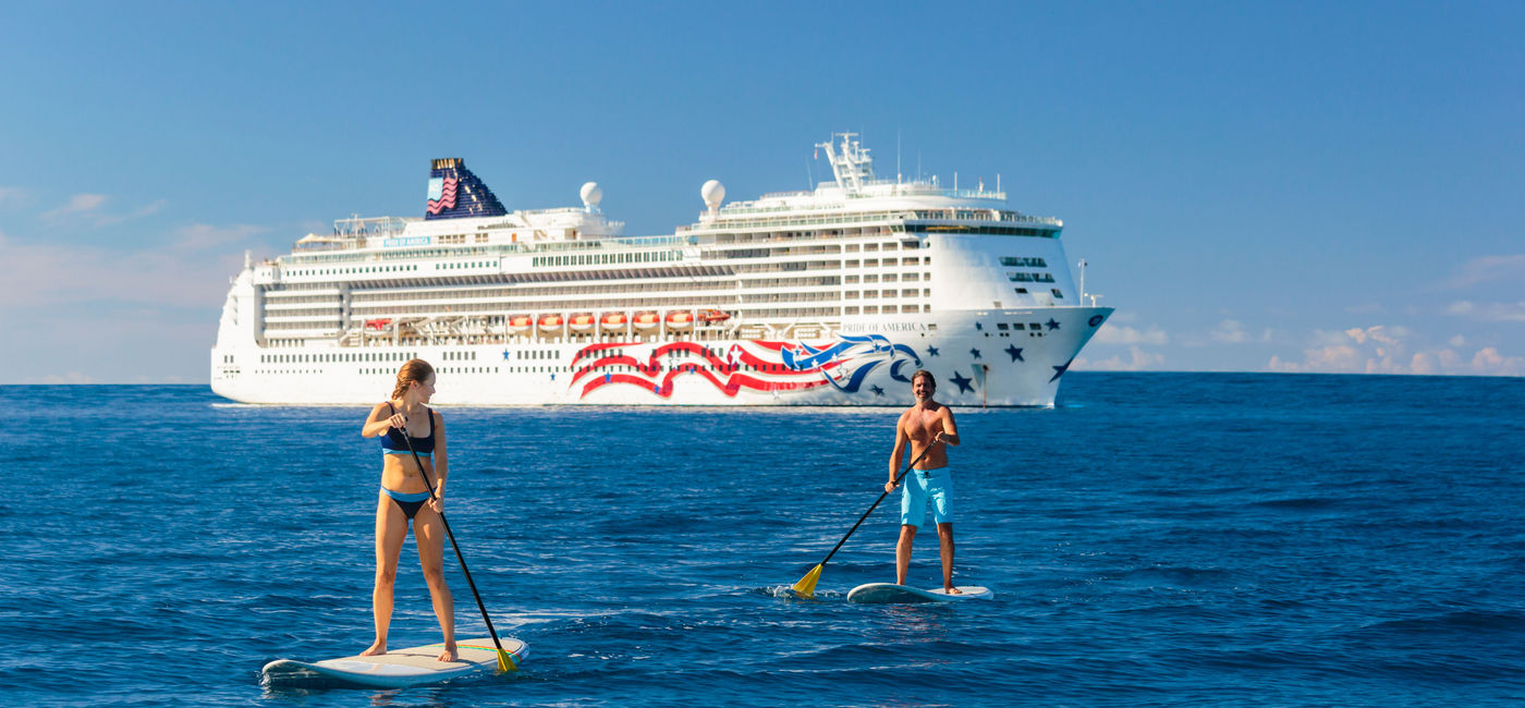Image: Two cruisers paddleboard in front of NCL's Pride of America ship in Hawaii. (photo via NCL) ((photo via NCL))
