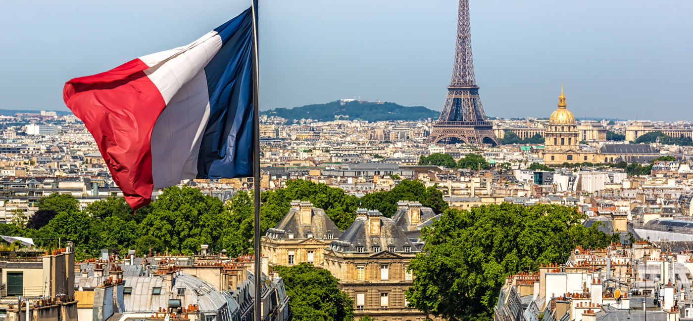 Image: The French Flag waving with Paris and the Eiffel Tower in the background. (photo via iStock/Getty Images Plus/Querbeet)