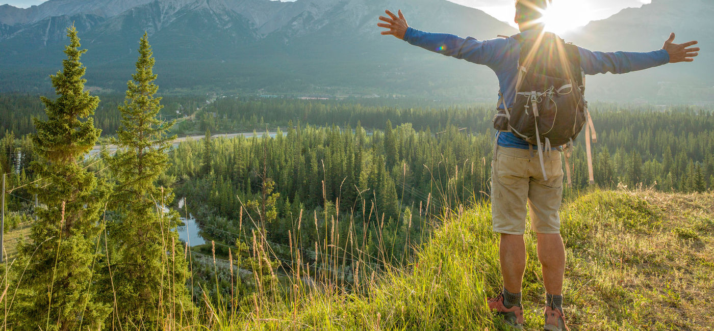 Image: Nature hiker with arms outstetched over a forested mountainscape. (photo via iStock/Getty Images E+/AscentXmedia)