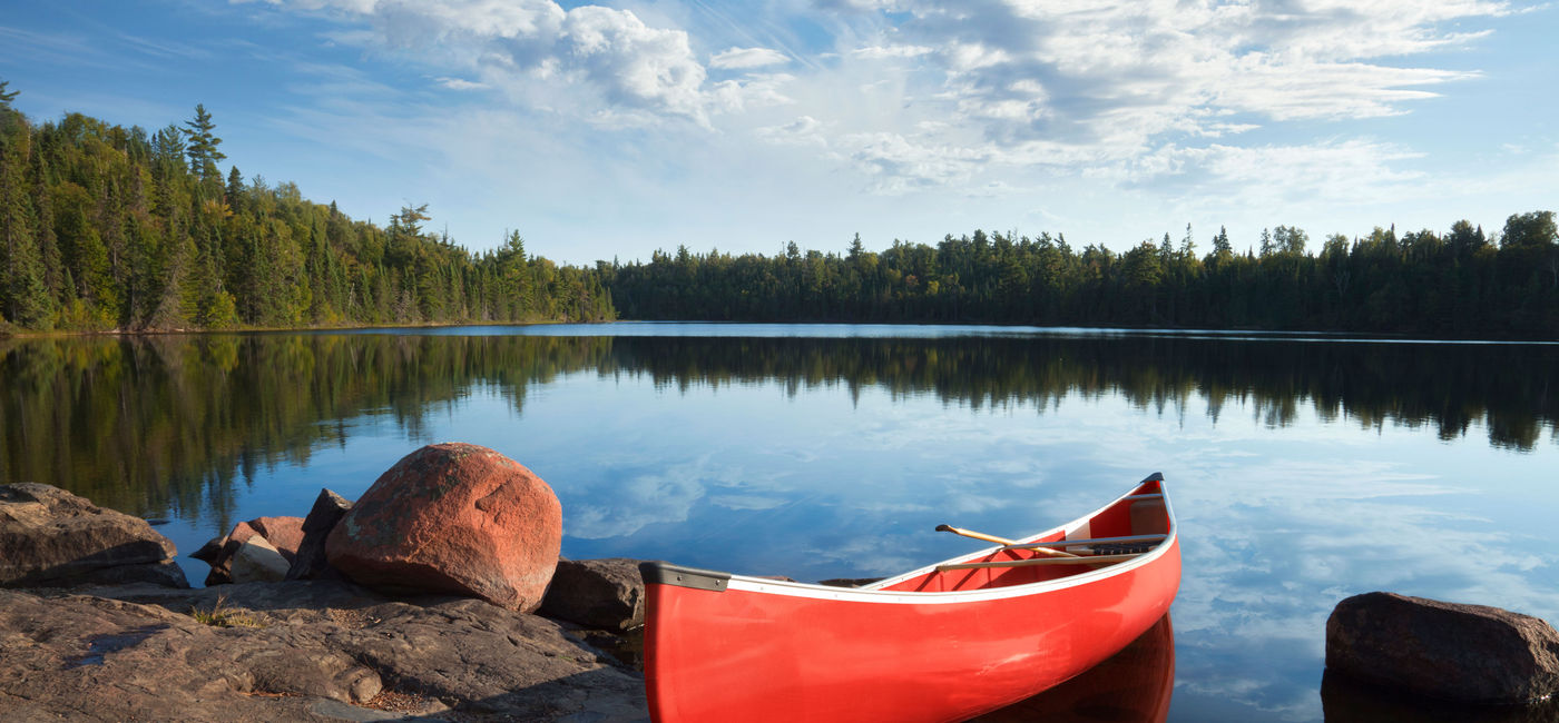Photo: A red canoe rests on a rocky shore of a calm blue lake in the Boundary Waters of Minnesota (Photo via Willard / iStock / Getty Images Plus)