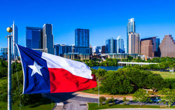 Texas flag flying in front of Austin Texas downtown skyline cityscape sunny perfect day (photo via RoschetzkyIstockPhoto / iStock / Getty Images Plus)