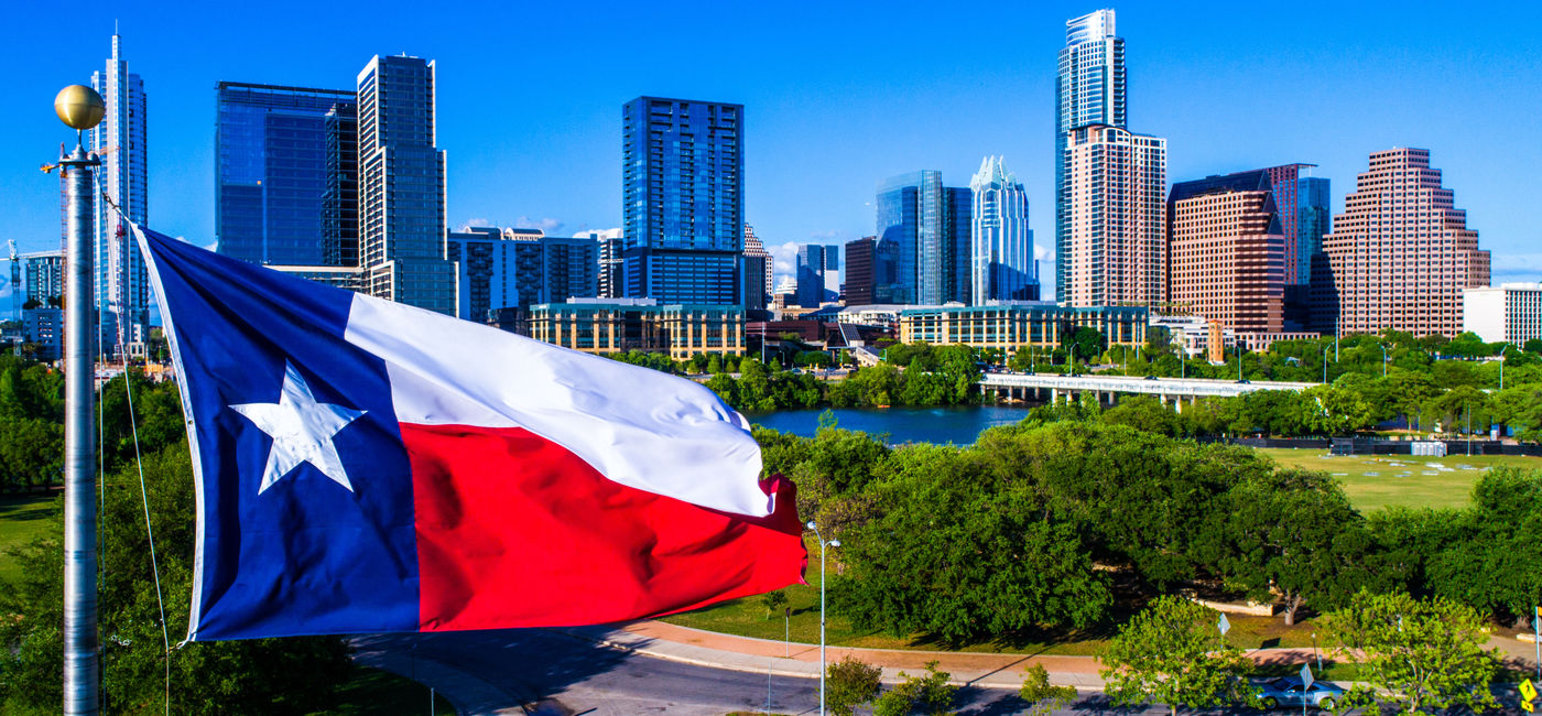 Image: Texas flag flying in front of Austin Texas downtown skyline cityscape sunny perfect day (photo via RoschetzkyIstockPhoto / iStock / Getty Images Plus)