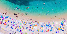 People bathing in the sun at the beach, aerial view with clear blue water and sandy beach. Corfu island Kerkyra, Greece (photo via CalinStan/iStock/Getty Images Plus)