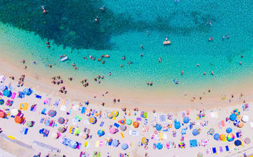 People bathing in the sun at the beach, aerial view with clear blue water and sandy beach. Corfu island Kerkyra, Greece (photo via CalinStan/iStock/Getty Images Plus)