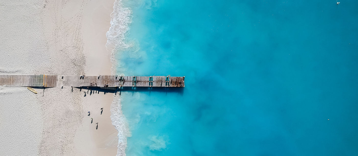 Drone photo of pier in Grace Bay, Providenciales, Turks and Caicos. The caribbean blue sea and white sandy beaches can be seen (photo via JoaoBarcelos / iStock / Getty Images Plus)