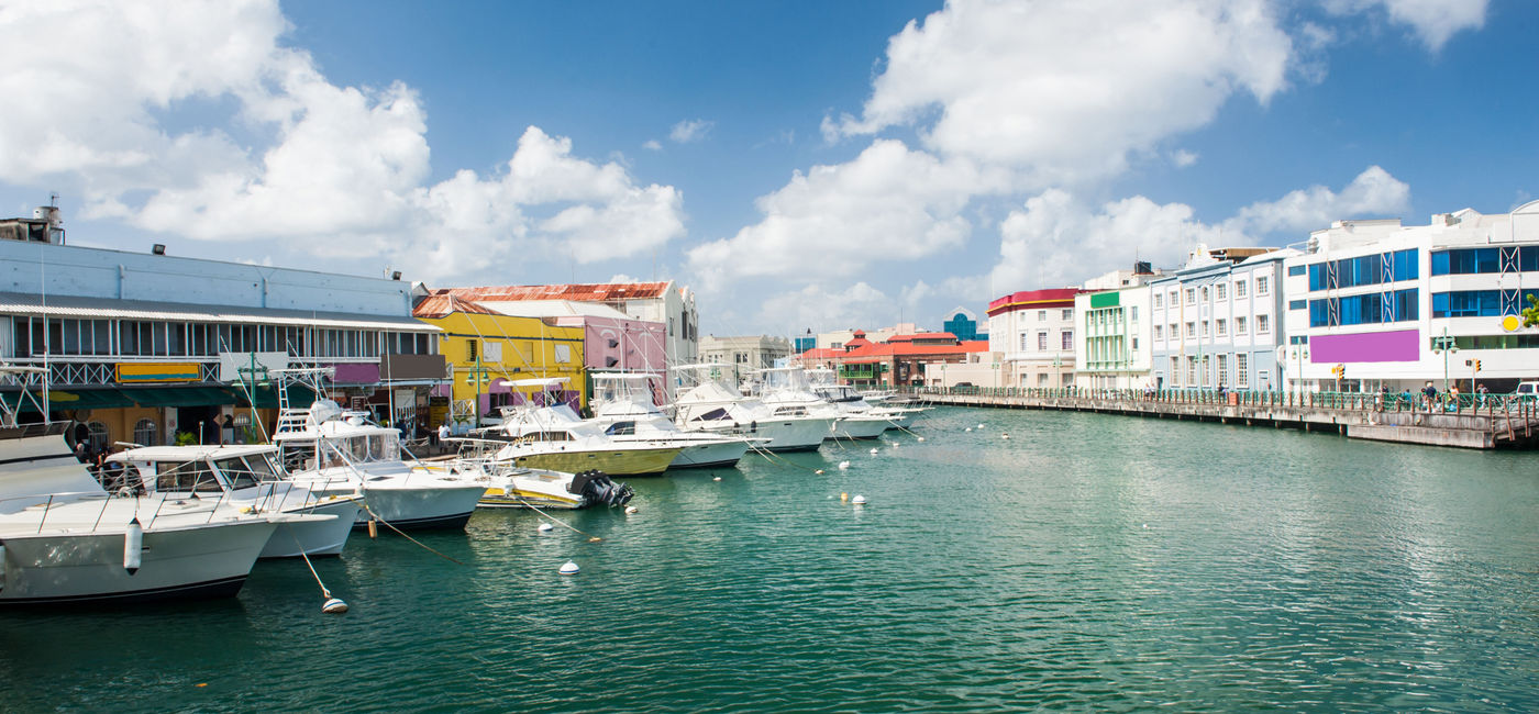 Image: Main water canal with ships and shops in Bridgetown, capital of Barbados. Caribbean (photo via Fyletto / iStock / Getty Images Plus)