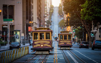 Classic view of historic traditional Cable Cars riding on famous California Street in beautiful early morning light at sunrise in summer, San Francisco, California, USA (photo via bluejayphoto / iStock / Getty Images Plus)