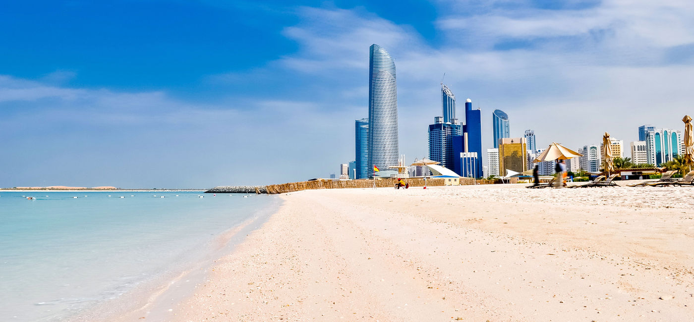 Image: sunny beach and cityscape in Abu Dhabi, UAE (photo via vlarub/iStock/Getty Images Plus)