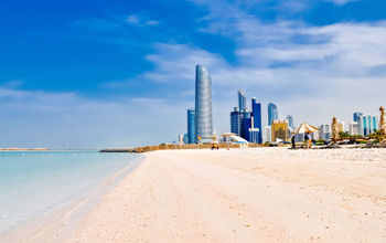 sunny beach and cityscape in Abu Dhabi, UAE (photo via vlarub/iStock/Getty Images Plus)