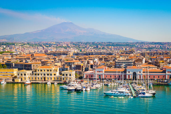 Catania Sicily, Italy Beautiful view of Catania cruise port with smoking volcano Etna in the background. (Photo via NAPA74 / iStock / Getty Images Plus)