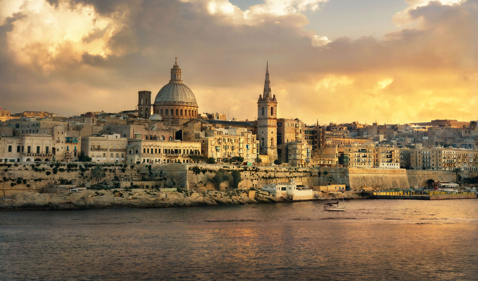 Panoramic view of Valletta at sunset with Carmelite Church dome and St. Pauls Anglican Cathedral. Malta (photo via Bareta / iStock / Getty Images Plus)