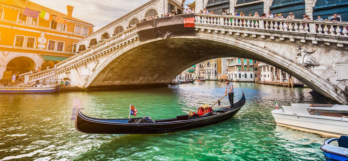 Image: Beautiful view of traditional Gondola on famous Canal Grande with Rialto Bridge at sunset in Venice, Italy with retro vintage Instagram style filter and lens flare effect. (photo via bluejayphoto / iStock / Getty Images Plus)
