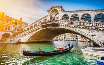 Beautiful view of traditional Gondola on famous Canal Grande with Rialto Bridge at sunset in Venice, Italy with retro vintage Instagram style filter and lens flare effect. (photo via bluejayphoto / iStock / Getty Images Plus)
