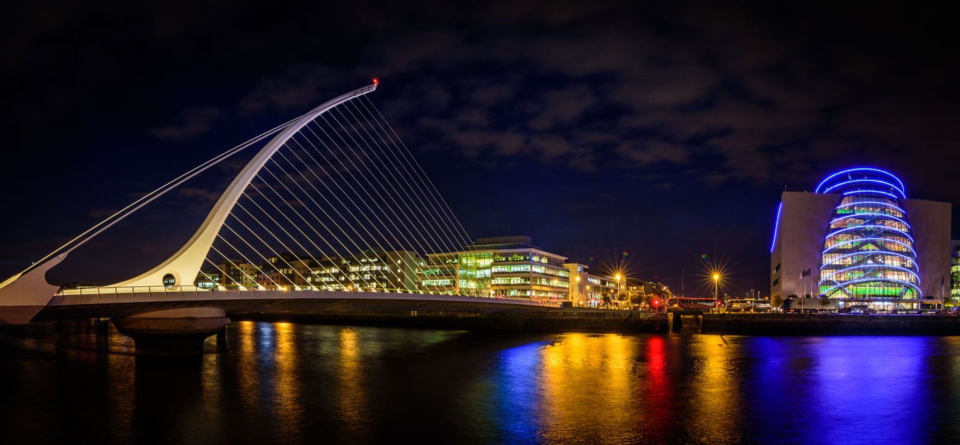 Image: Panorama of Dublin by night. River with citylights reflections. Samuel Beckett Bridge. (photo via muzzyco / iStock / Getty Images Plus)