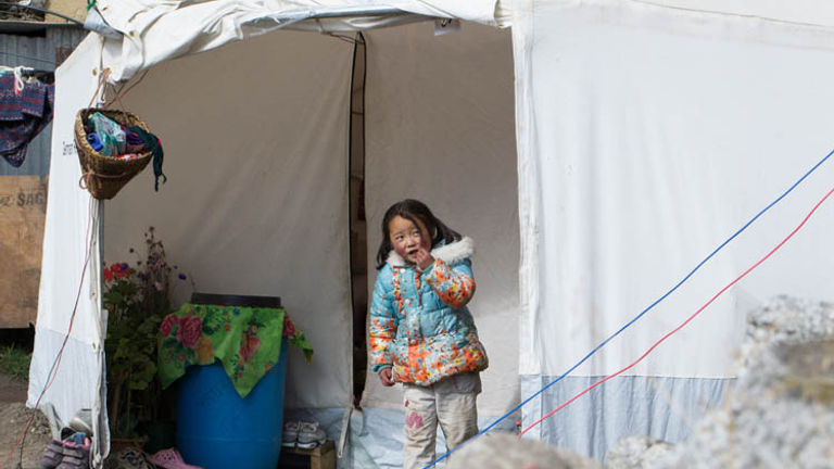 A young girl peeks out of a tent donated by an international aid group. // © 2015 Mindy Poder