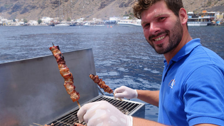 A captain plays chef, cooking up souvlaki onboard Santorini’s Lagoon 520 catamaran // © 2016 Tim Johnson