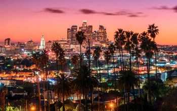 Beautiful sunset of Los Angeles downtown skyline and palm trees in foreground (Photo via choness / iStock / Getty Images Plus)