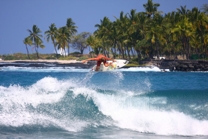 Surfer flying above wave crest with palm trees in background