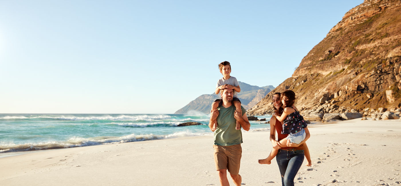 Image: Family travelers walking along the beach (Photo Credit: Courtesy AdobeStock)