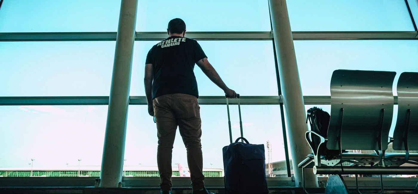 Image: A man watches out the window at an airport (Photo Credit: Photo by Victor Freitas on Pexels)