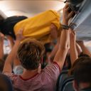 Airplane passengers pulling their carry-on items out of overhead luggage compartments.