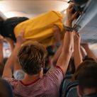 Airplane passengers pulling their carry-on items out of overhead luggage compartments.