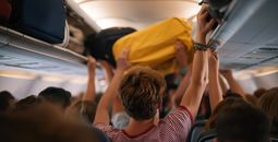 Airplane passengers pulling their carry-on items out of overhead luggage compartments.