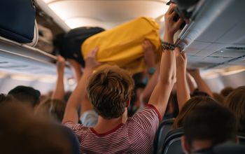 Airplane passengers pulling their carry-on items out of overhead luggage compartments.