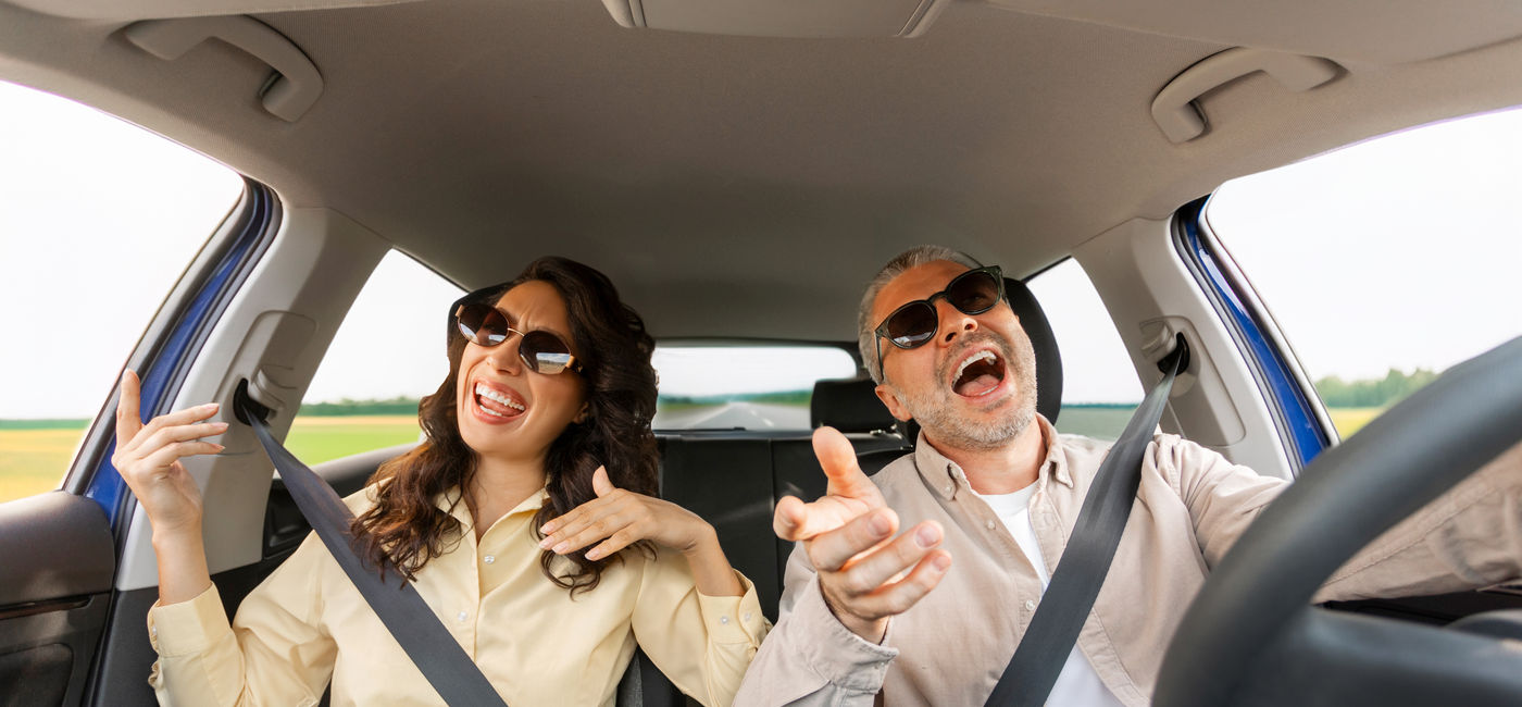 Image: Couple singing along to a road trip playlist. (Photo Credit: Adobe/Home-stock)