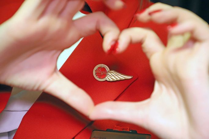 A woman forms the shape of a heart with her hands around a Virgin Atlantic pin. Virgin Atlantic, Virgin Atlantic Airways